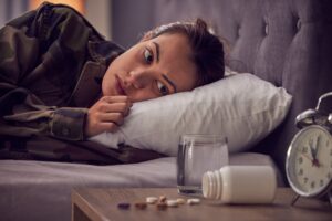 mujer con insomnio en su cama mirando el reloj y los medicamentos.